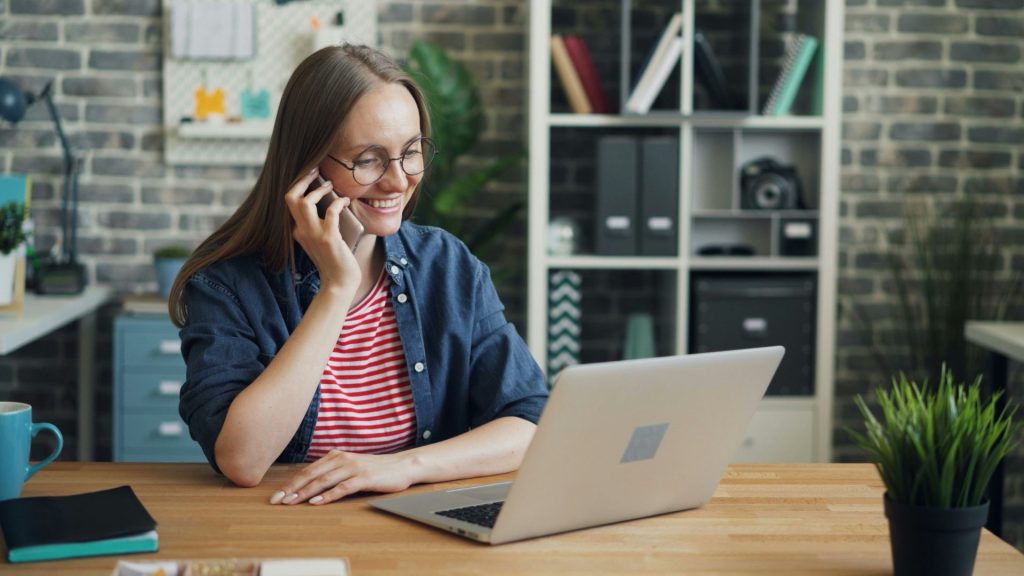 a woman talking on a cell phone while using a laptop